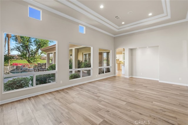 interior space with a towering ceiling, a tray ceiling, light hardwood / wood-style flooring, and ornamental molding