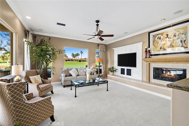 living room with ceiling fan, light colored carpet, ornamental molding, and a tiled fireplace