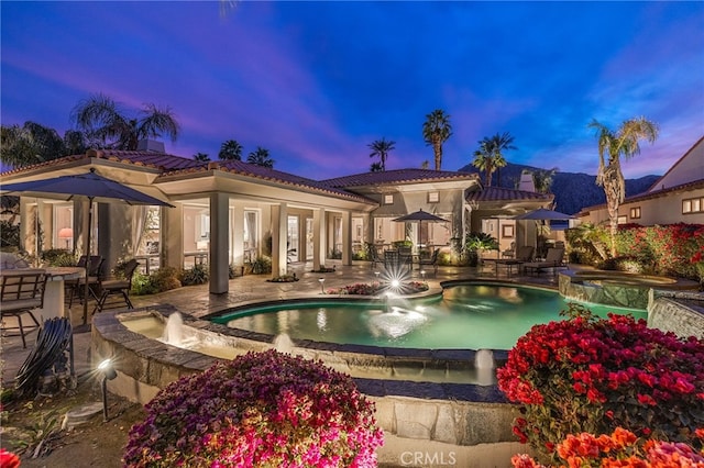 pool at dusk with pool water feature, an in ground hot tub, and a patio