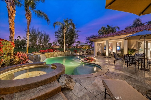 pool at dusk with an in ground hot tub and a patio area