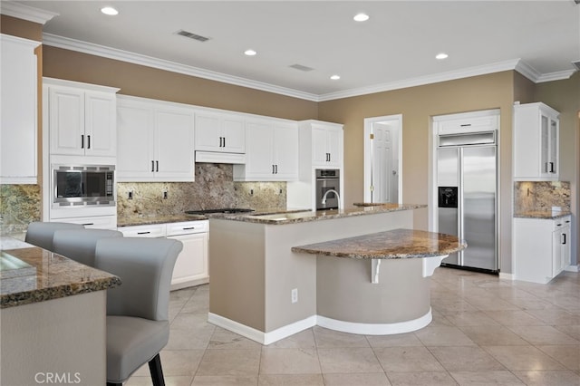 kitchen featuring white cabinets, decorative backsplash, built in appliances, and a breakfast bar area