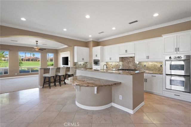 kitchen featuring a kitchen breakfast bar, a kitchen island with sink, white cabinetry, and appliances with stainless steel finishes