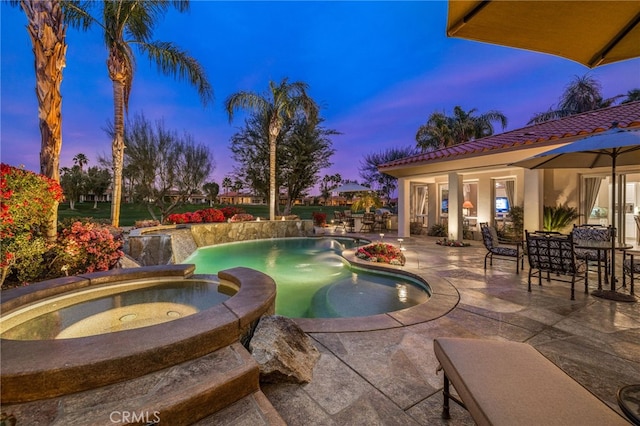 pool at dusk featuring a patio area and an in ground hot tub