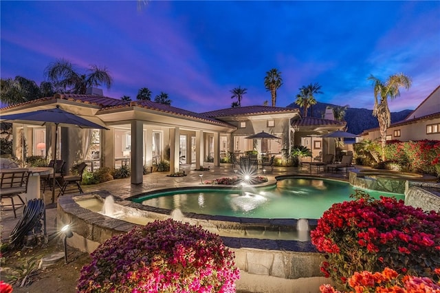 pool at dusk featuring an in ground hot tub, pool water feature, and a patio