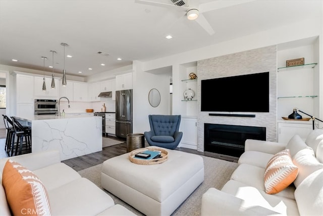 living room with light hardwood / wood-style flooring, built in shelves, a large fireplace, and ceiling fan