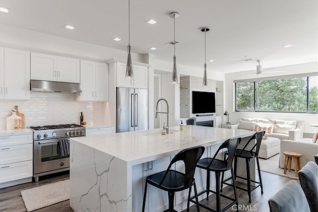 kitchen featuring high quality appliances, dark wood-type flooring, a center island with sink, sink, and white cabinets