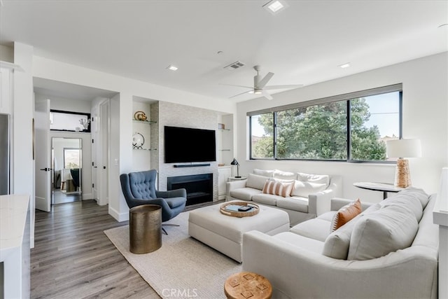 living room featuring ceiling fan, built in features, a large fireplace, and hardwood / wood-style floors