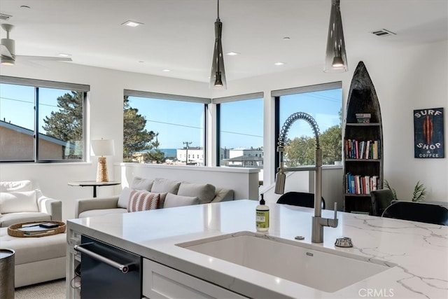 kitchen with white cabinets, light stone counters, sink, and hanging light fixtures