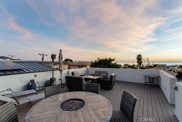 deck at dusk with an outdoor living space with a fire pit and a water view