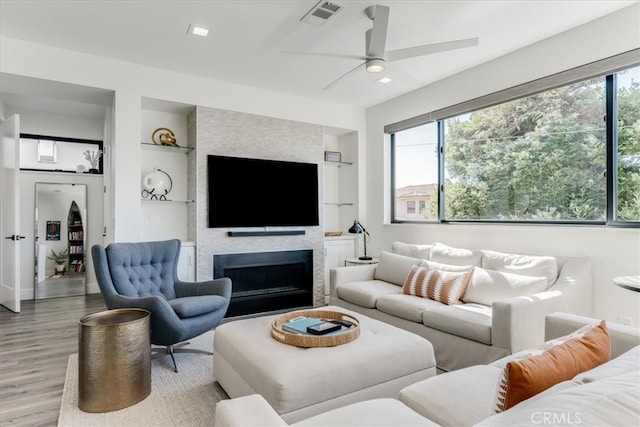 living room with a large fireplace, a healthy amount of sunlight, built in features, and light wood-type flooring