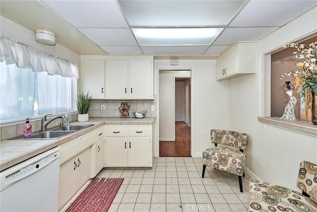 kitchen featuring sink, light tile patterned floors, dishwasher, white cabinetry, and tile counters