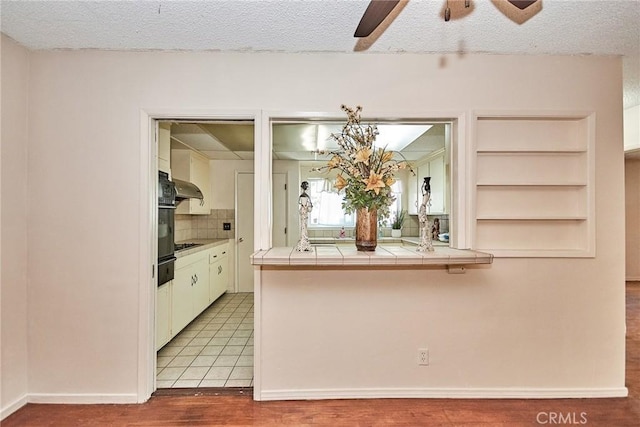 kitchen featuring ventilation hood, a textured ceiling, light hardwood / wood-style floors, and tile counters