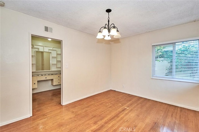 unfurnished room with a chandelier, wood-type flooring, a textured ceiling, and built in desk