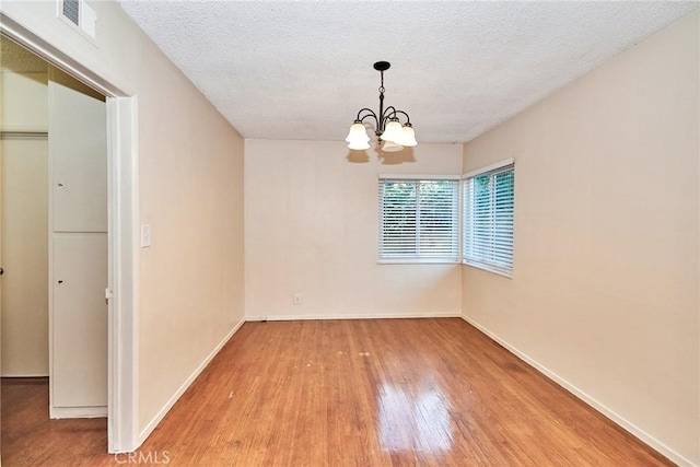 empty room featuring wood-type flooring, a textured ceiling, and an inviting chandelier