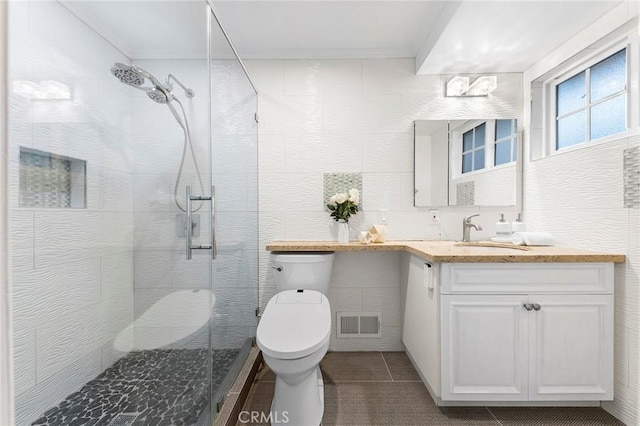 bathroom with vanity, a shower with door, tile patterned floors, toilet, and tile walls