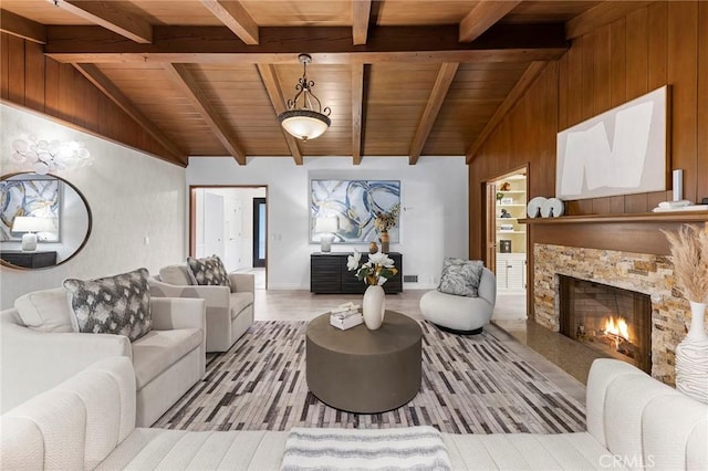 living room featuring light wood-type flooring, wooden ceiling, a fireplace, vaulted ceiling with beams, and wood walls