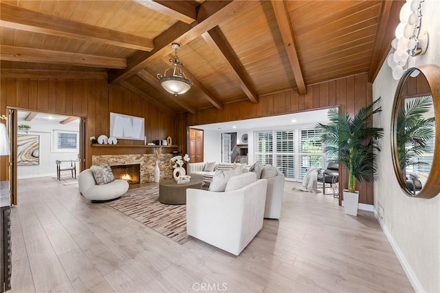 living room with vaulted ceiling with beams, light hardwood / wood-style floors, a stone fireplace, and wooden ceiling