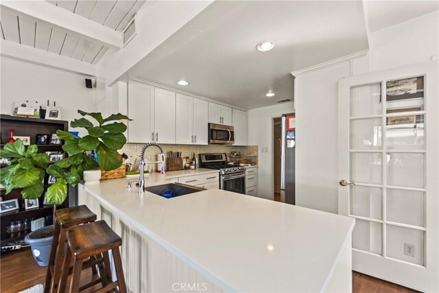 kitchen with kitchen peninsula, beam ceiling, appliances with stainless steel finishes, dark wood-type flooring, and sink