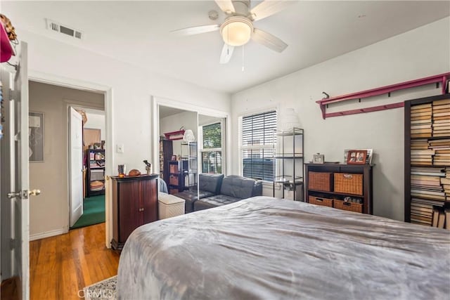 bedroom with a closet, visible vents, a ceiling fan, wood finished floors, and baseboards