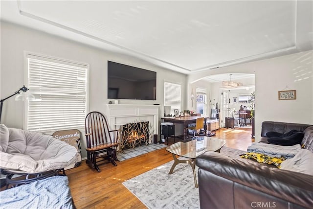 living room with a fireplace with flush hearth, arched walkways, a raised ceiling, and wood finished floors