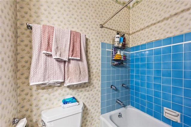 bathroom with tub / shower combination, toilet, and wallpapered walls