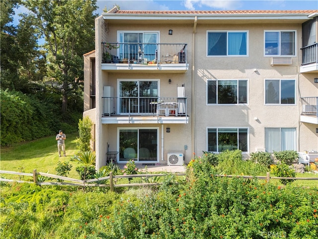 rear view of house featuring ac unit, a lawn, and a balcony