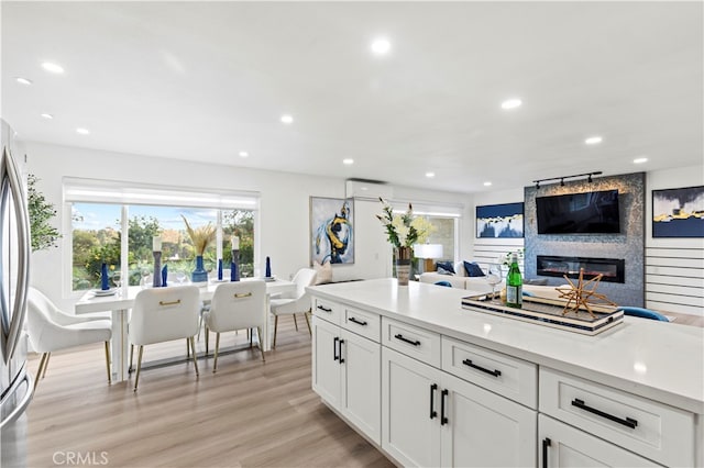 kitchen featuring a wall unit AC, appliances with stainless steel finishes, white cabinetry, a fireplace, and light hardwood / wood-style floors