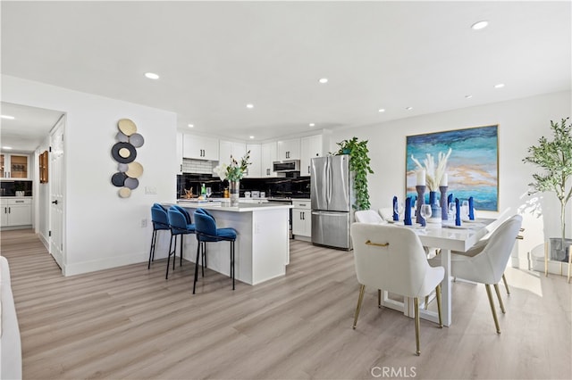 kitchen with decorative backsplash, light hardwood / wood-style flooring, stainless steel appliances, a kitchen bar, and white cabinetry