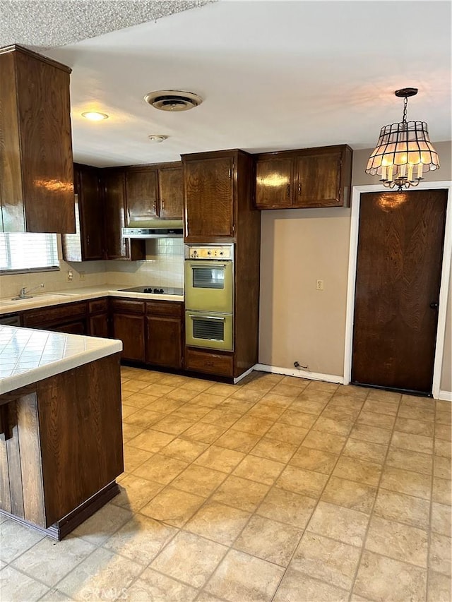 kitchen with sink, hanging light fixtures, black electric cooktop, tile counters, and dark brown cabinetry