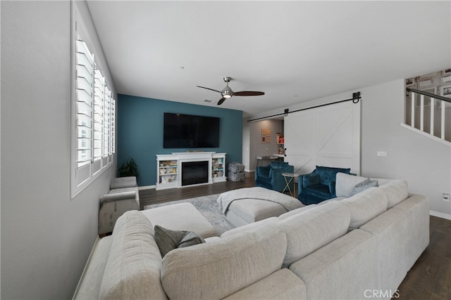 living room with dark wood-type flooring, ceiling fan, a fireplace, and a barn door