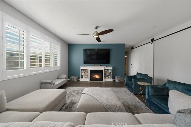 living area with a barn door, a ceiling fan, wood finished floors, and a lit fireplace