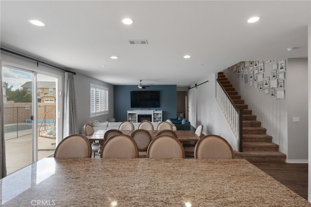 dining room with ceiling fan, a barn door, and dark hardwood / wood-style floors