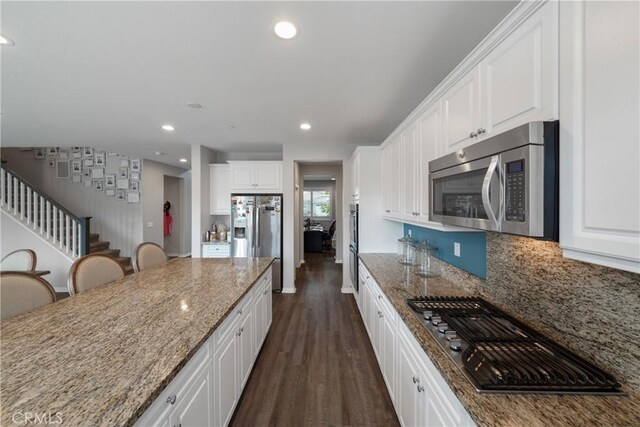 kitchen with appliances with stainless steel finishes, a breakfast bar, white cabinetry, dark stone countertops, and dark hardwood / wood-style floors