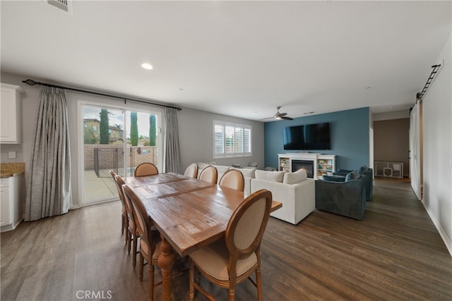 dining space with dark wood-type flooring, ceiling fan, a stone fireplace, and a barn door