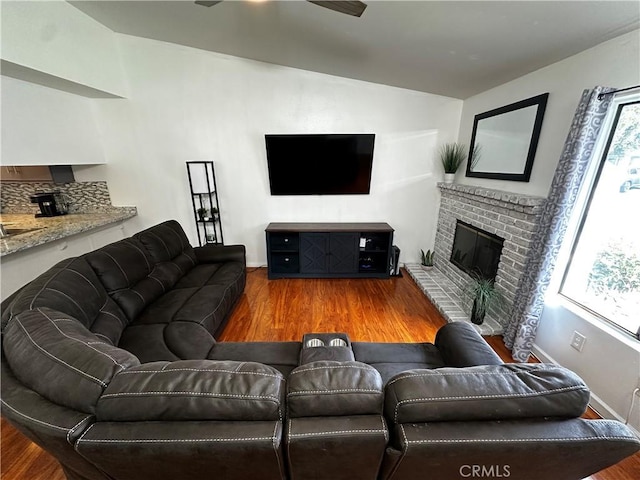 living room featuring hardwood / wood-style flooring, a brick fireplace, ceiling fan, and sink