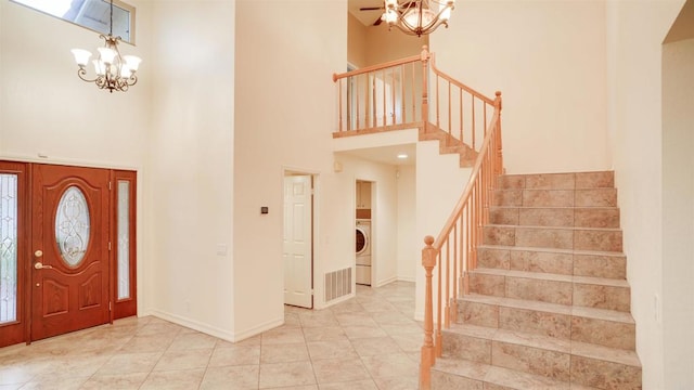 tiled entrance foyer with a notable chandelier, washer / clothes dryer, and a high ceiling