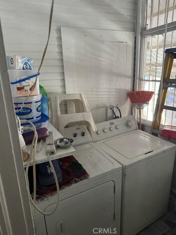 clothes washing area featuring separate washer and dryer, a wealth of natural light, and wooden walls