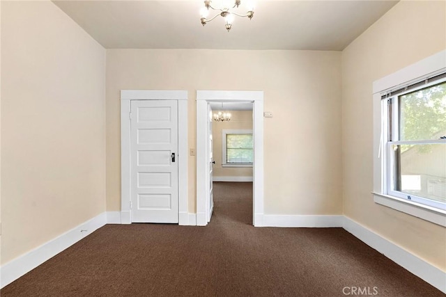 unfurnished room featuring dark carpet and an inviting chandelier