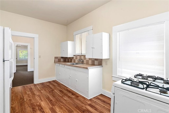 kitchen with white appliances, wood-type flooring, sink, tasteful backsplash, and white cabinetry