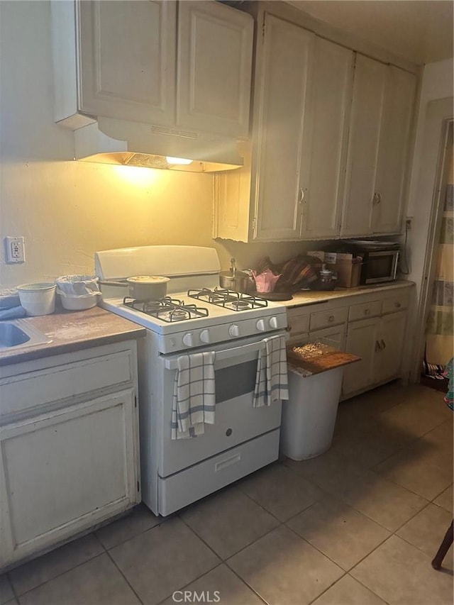 kitchen featuring white cabinets, gas range gas stove, light tile patterned flooring, and extractor fan