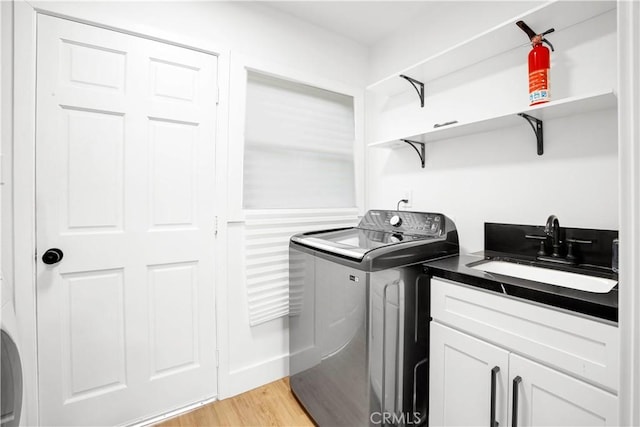 clothes washing area with cabinets, sink, light hardwood / wood-style flooring, and washing machine and dryer