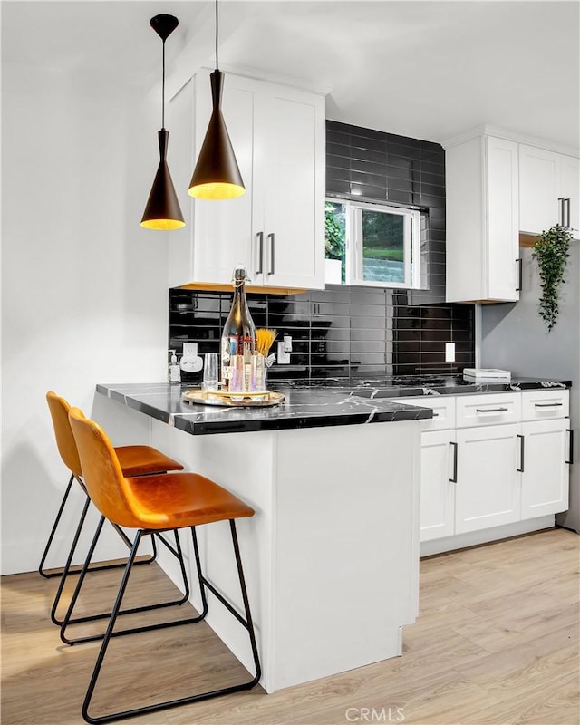 kitchen with decorative light fixtures, white cabinets, backsplash, and light wood-type flooring