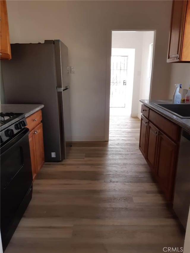 kitchen with black electric range, light hardwood / wood-style flooring, stainless steel dishwasher, and sink