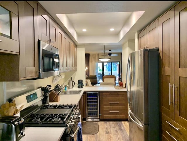 kitchen with stainless steel appliances, wine cooler, light hardwood / wood-style flooring, pendant lighting, and a tray ceiling