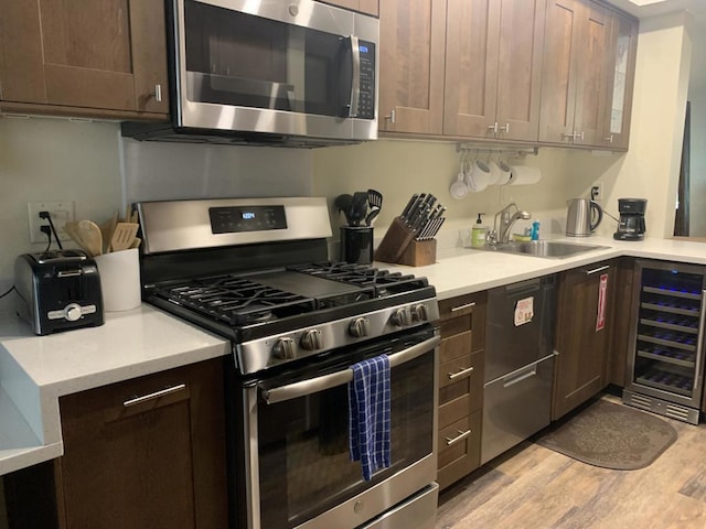 kitchen with sink, appliances with stainless steel finishes, light hardwood / wood-style floors, dark brown cabinetry, and beverage cooler