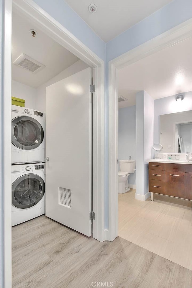 clothes washing area with laundry area, visible vents, light wood-style flooring, and stacked washing maching and dryer