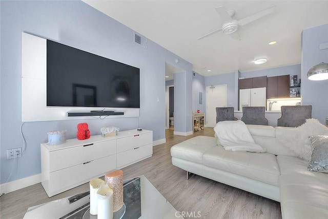 living room with light wood-style floors, visible vents, baseboards, and a ceiling fan