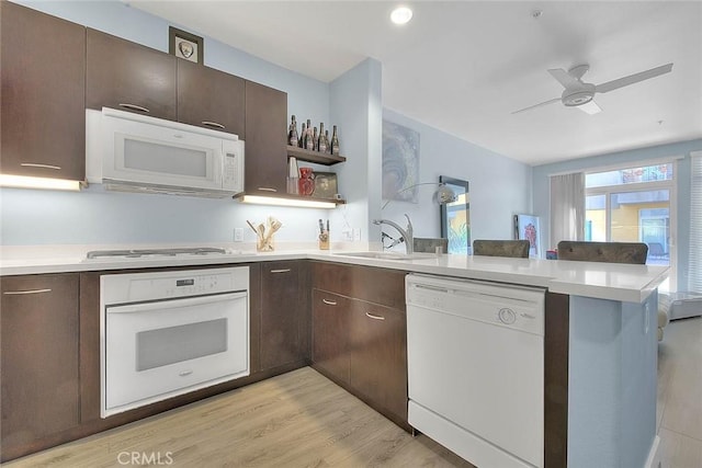 kitchen featuring light countertops, a sink, dark brown cabinets, white appliances, and a peninsula