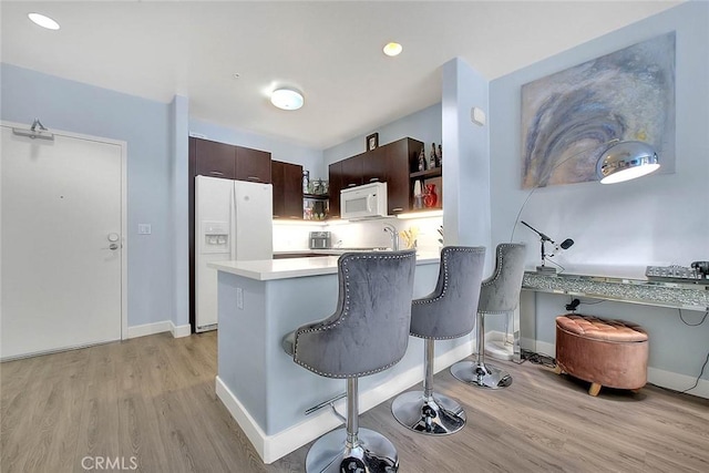 kitchen featuring white appliances, light wood-type flooring, dark brown cabinetry, and a kitchen breakfast bar