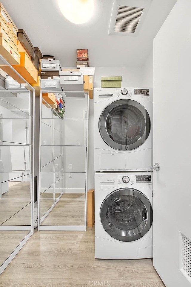 laundry area featuring laundry area, visible vents, stacked washing maching and dryer, and wood finished floors